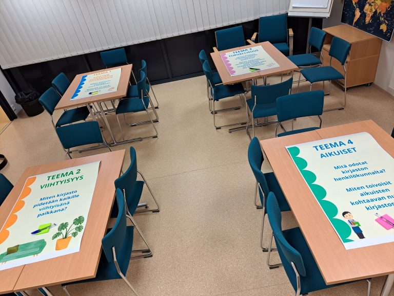 Kuvassa on pöytiä, joilla on työpajoissa käytettävää materiaalia.